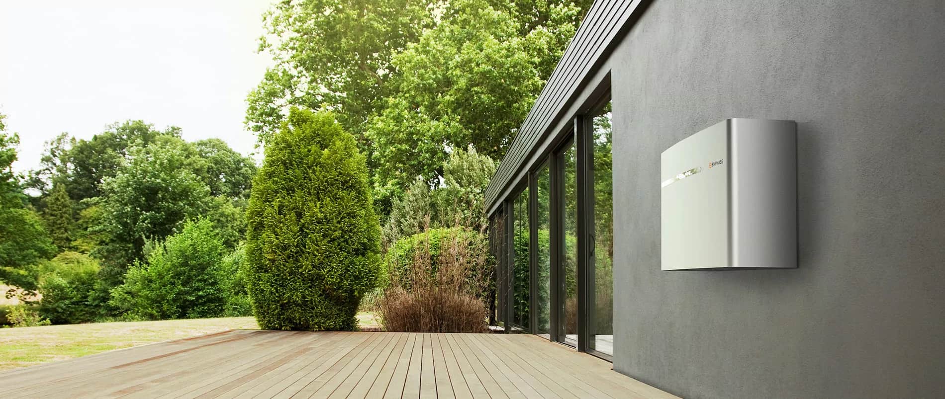 Enphase IQ Battery mounted on a concrete wall outside a modern house