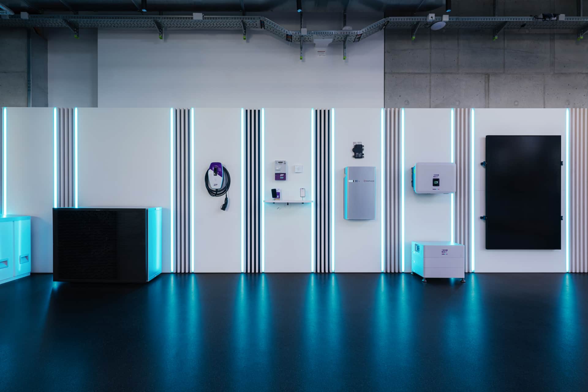 Moderni esittelytila, jossa valaistut paneelit esittelevät erilaisia elektronisia laitteita ja varusteita tyylikkään, futuristisen taustan edessä.