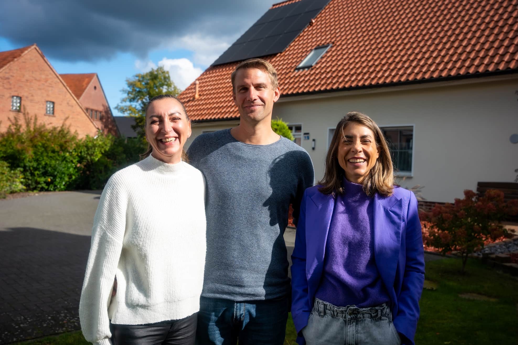 Drei Menschen stehen vor einem Haus mit einer PV-Anlage