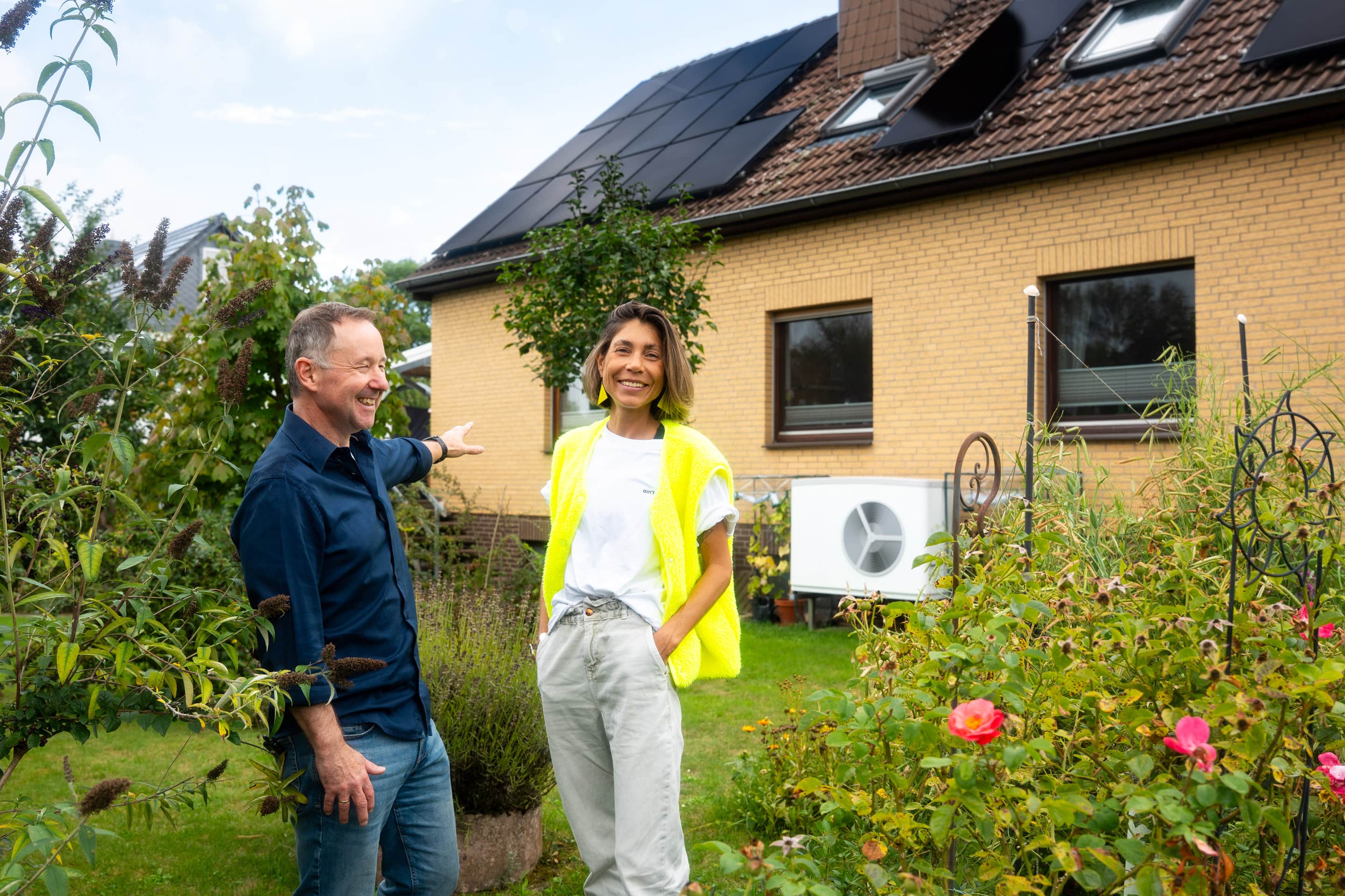 Carsten Klinge steht mit Sophia Rödiger von 1KOMMA5° vor seinem Haus, im Hintergrund erkennt man die PV-Anlage und seine neue Wärmepumpe