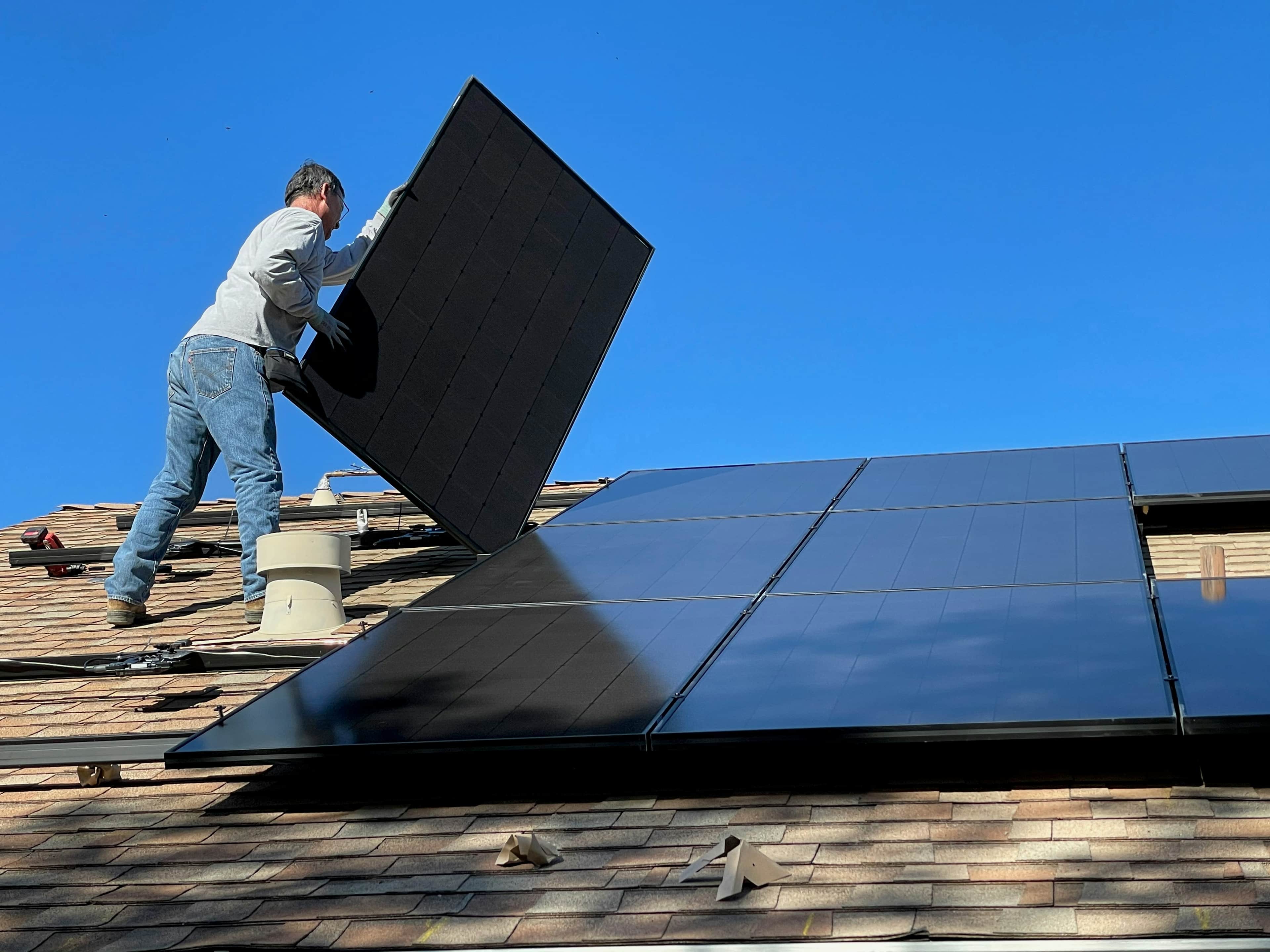 an installer on a roof carrying a black solar panel