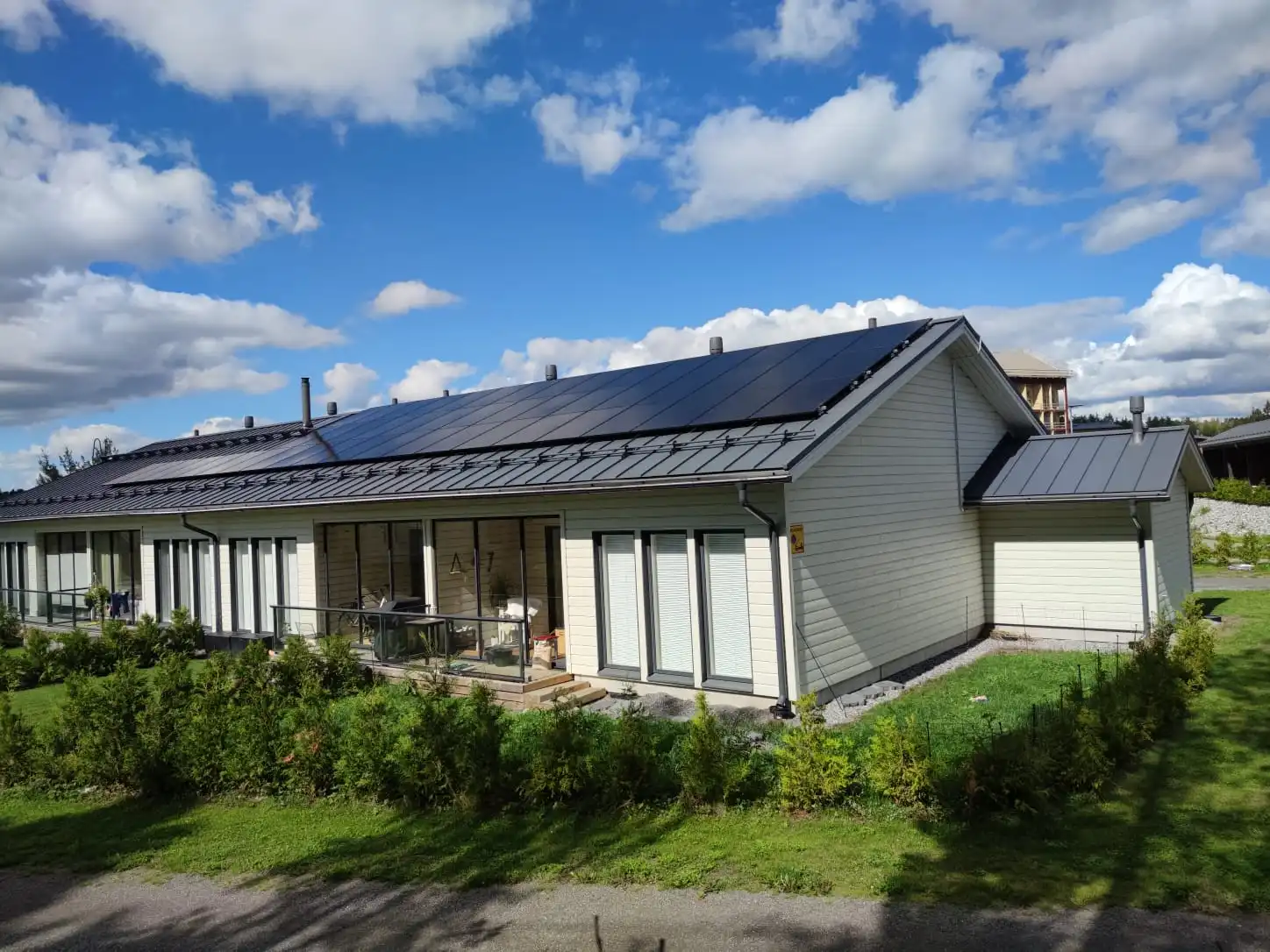 Rivitaloja, joiden katolla on aurinkopaneelit, vihreän nurmikon ja pensaiden ympäröimänä osittain pilvisen sinisen taivaan alla.