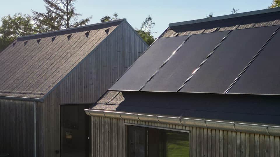 Modernit puiset rakennukset, joiden katoilla on tyylikkäät tummat aurinkopaneelit, puiden ja kirkkaan taivaan ympäröimänä.