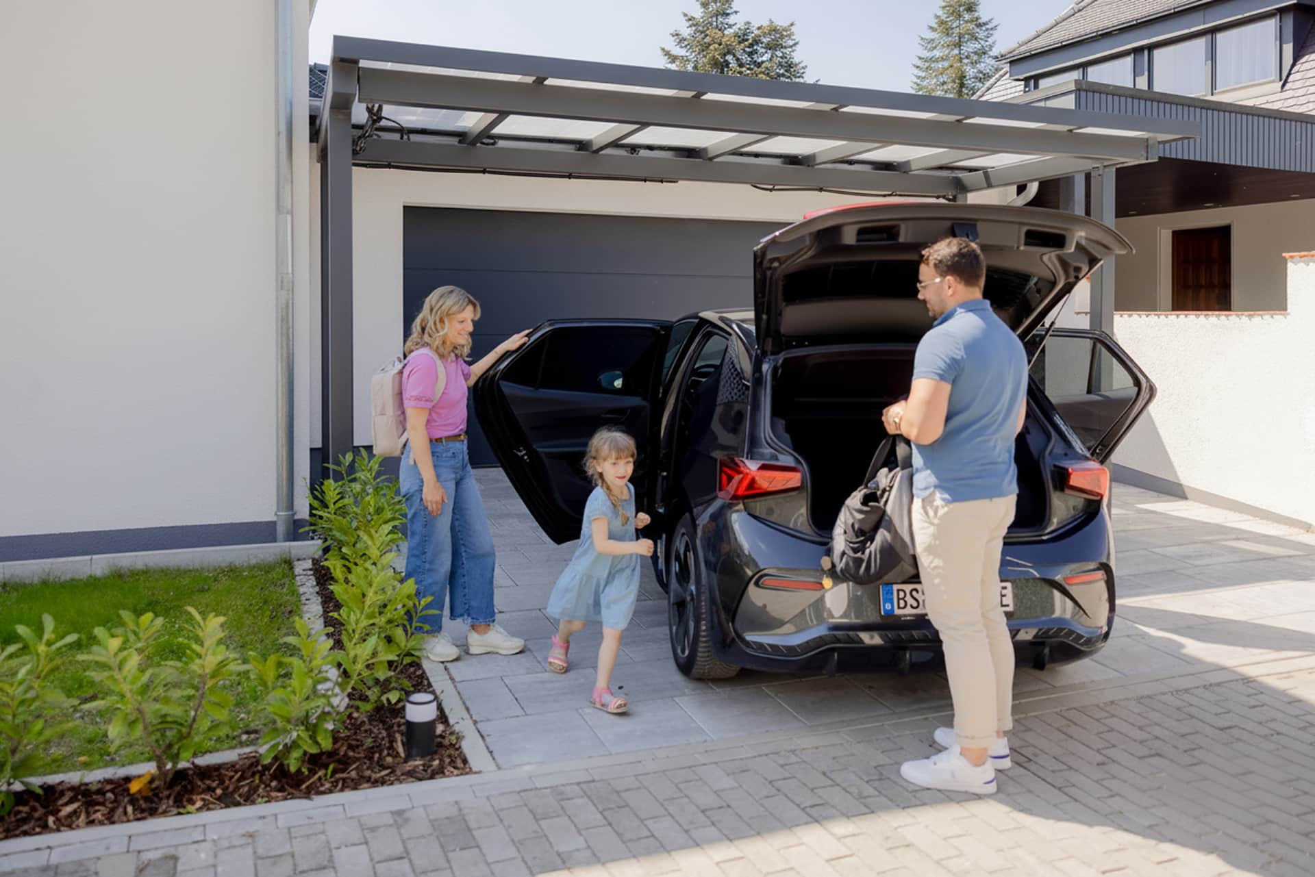 Familie stiger ud af bilen der er parkeret under carport med solceller