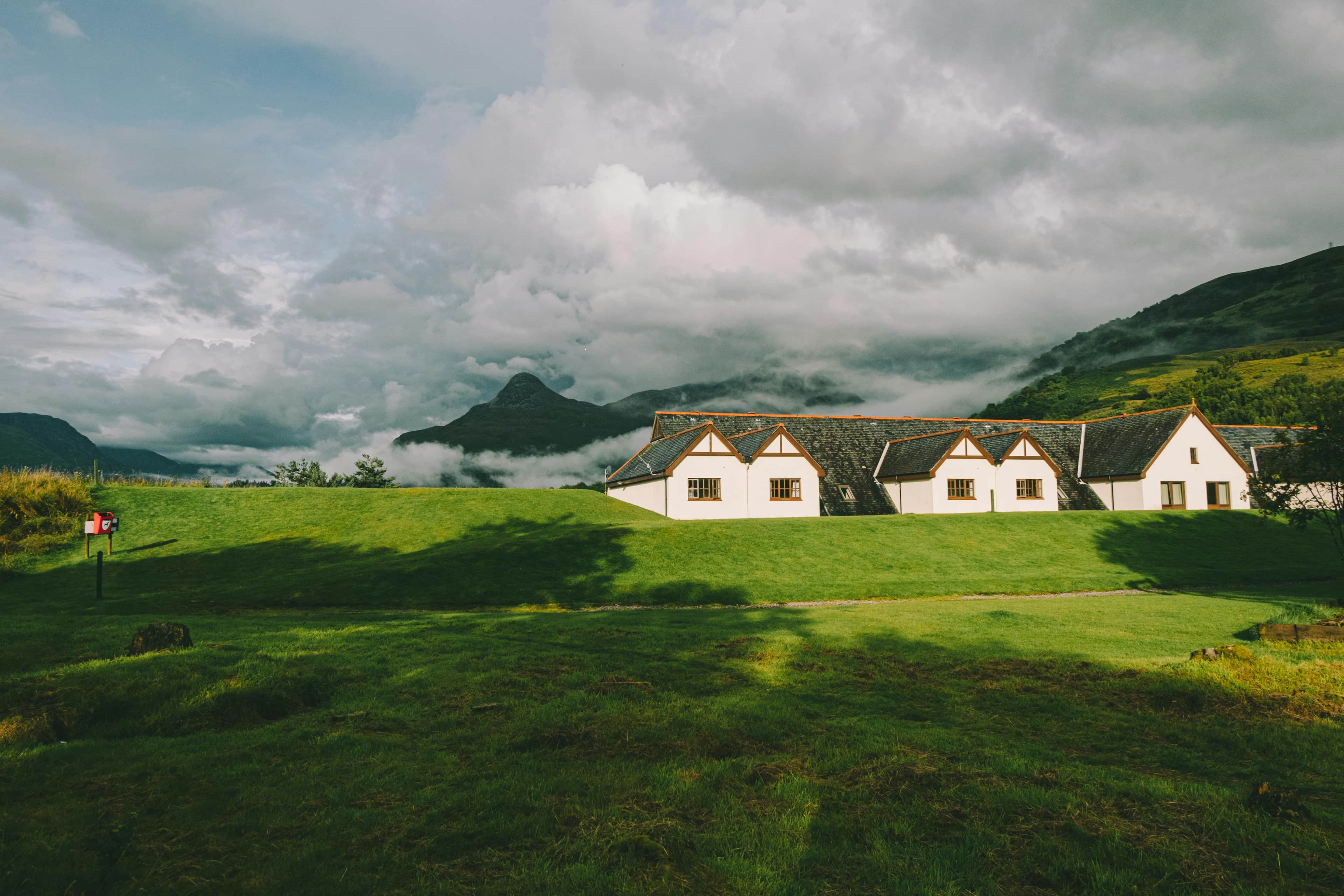 white cottage in a picturesque countryside, surrounded by green fields and distant mountains