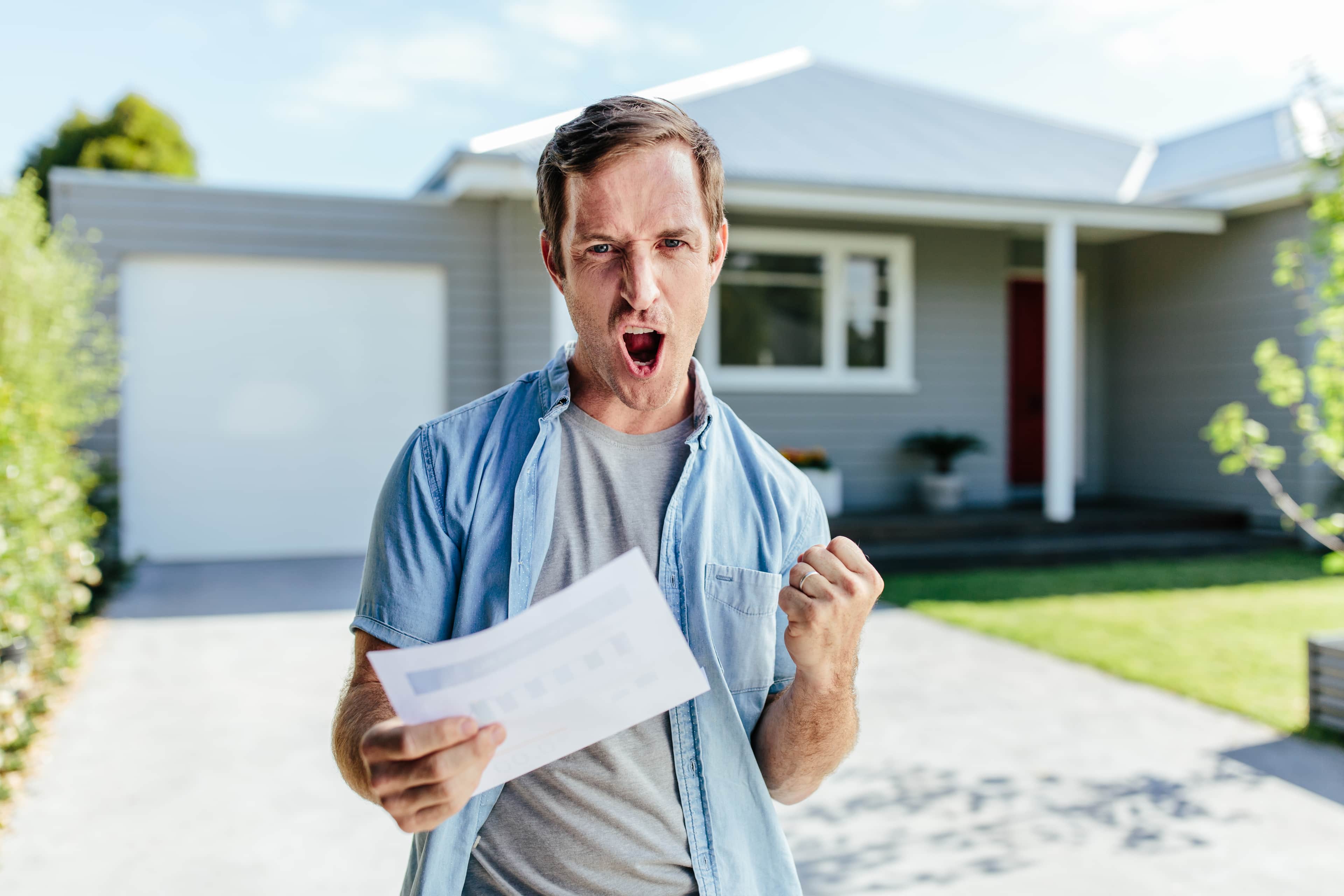 happy man holding his power bill with his house on the background