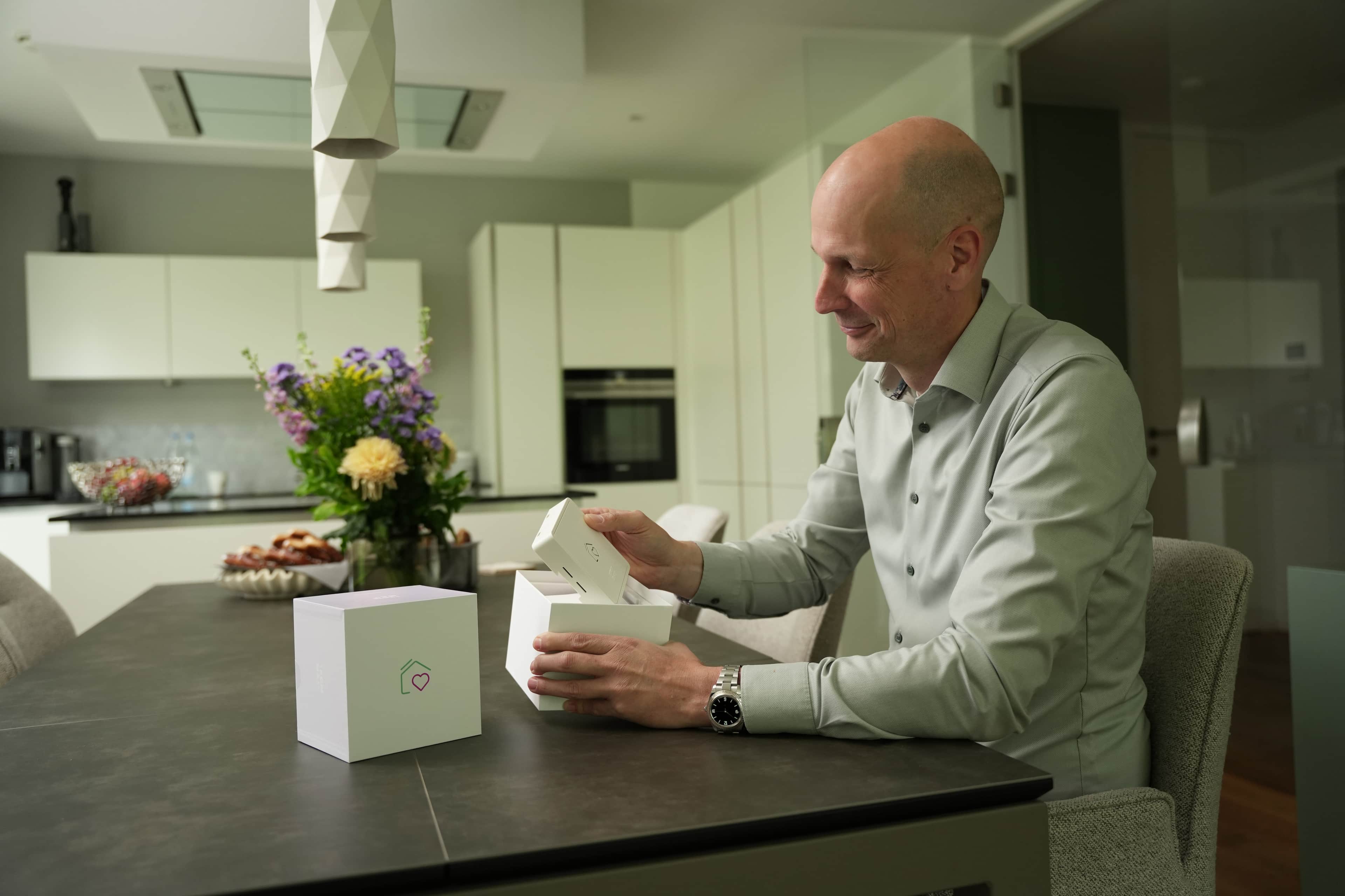 Ein Mann sitzt am Küchentisch und öffnet ein Paket mit der Heartbeat-Box