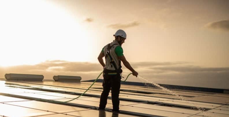 a technician sprays water on solar panels during sunset