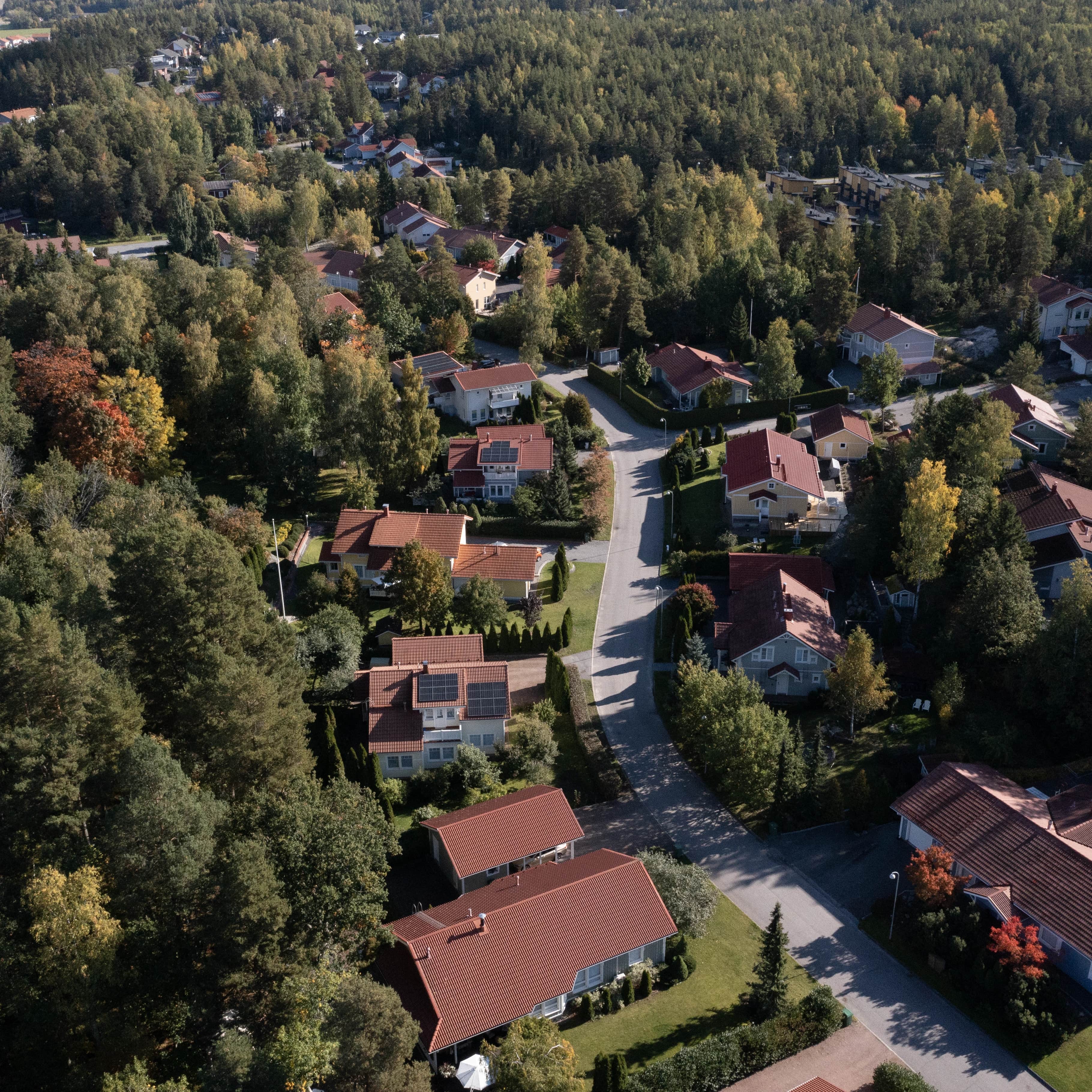 Ilmakuva esikaupunkialueesta, jossa on punakattoisia taloja, mutkittelevia puiden reunustamia katuja ja tiheä ympäröivä metsä.