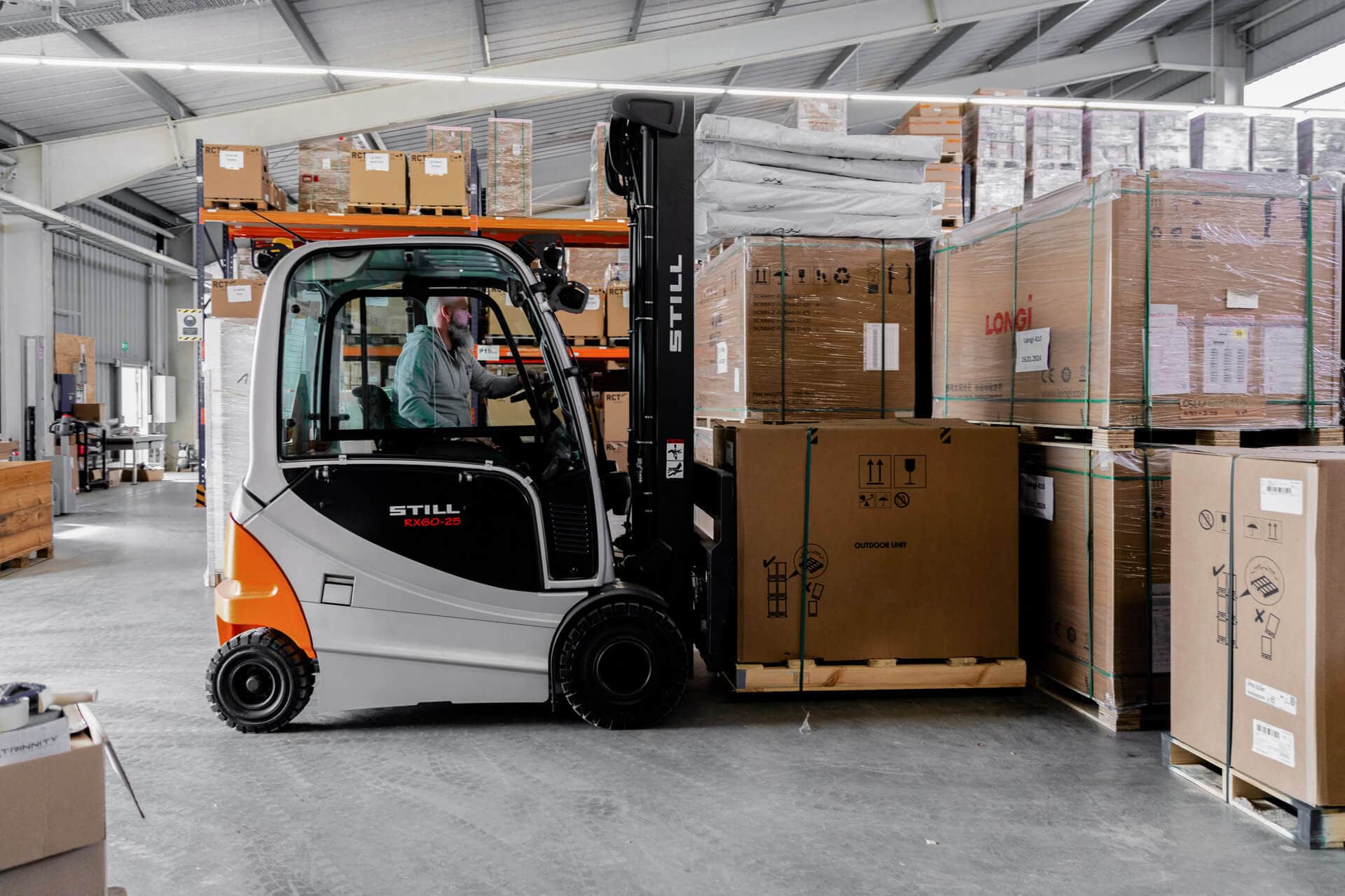 Varastotyöntekijä käyttää trukkia siirtäen pinottuja pahvilavoja valoisassa teollisuusvarastossa.