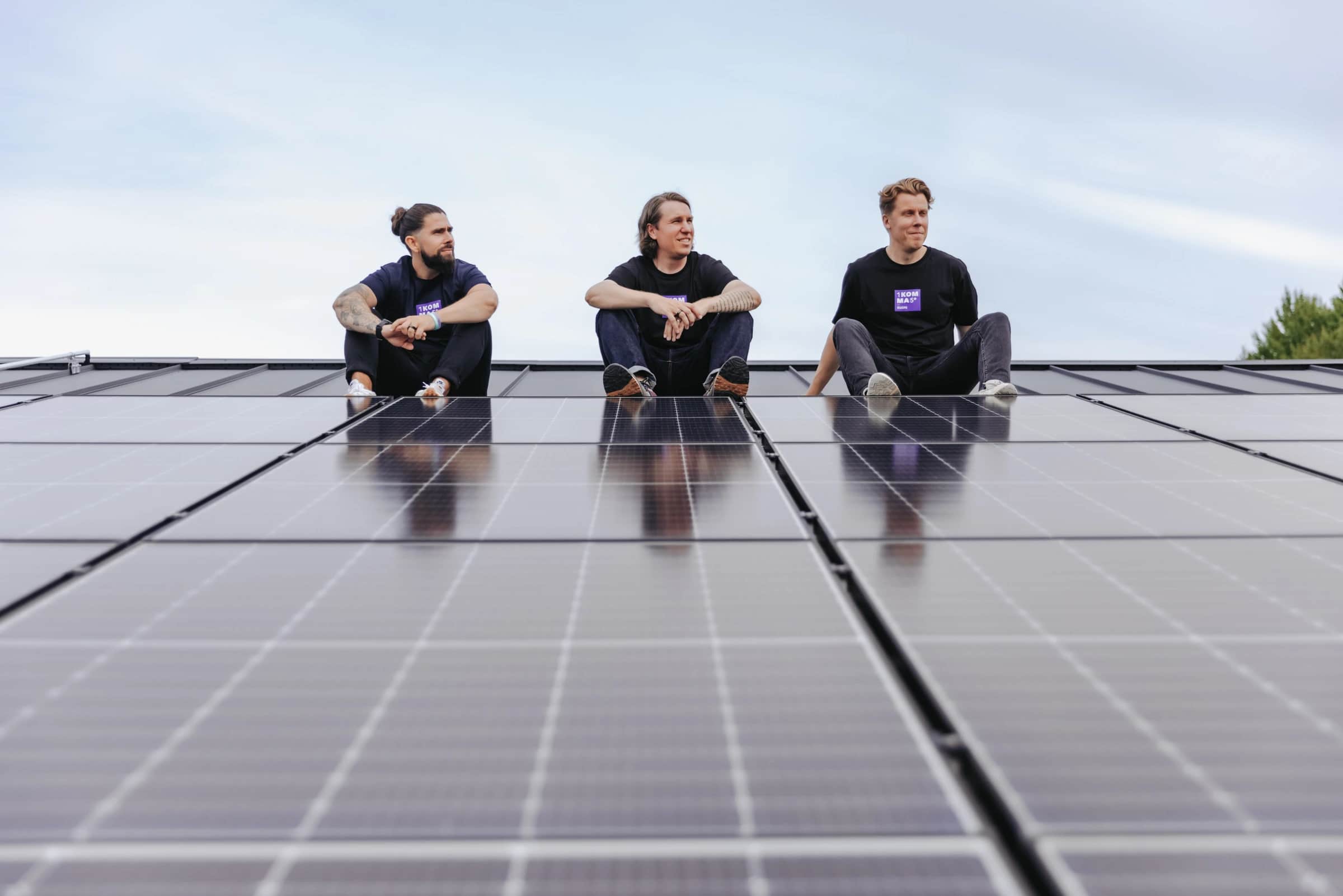Kolme yrittäjää katolla aurinkopaneeleiden takana