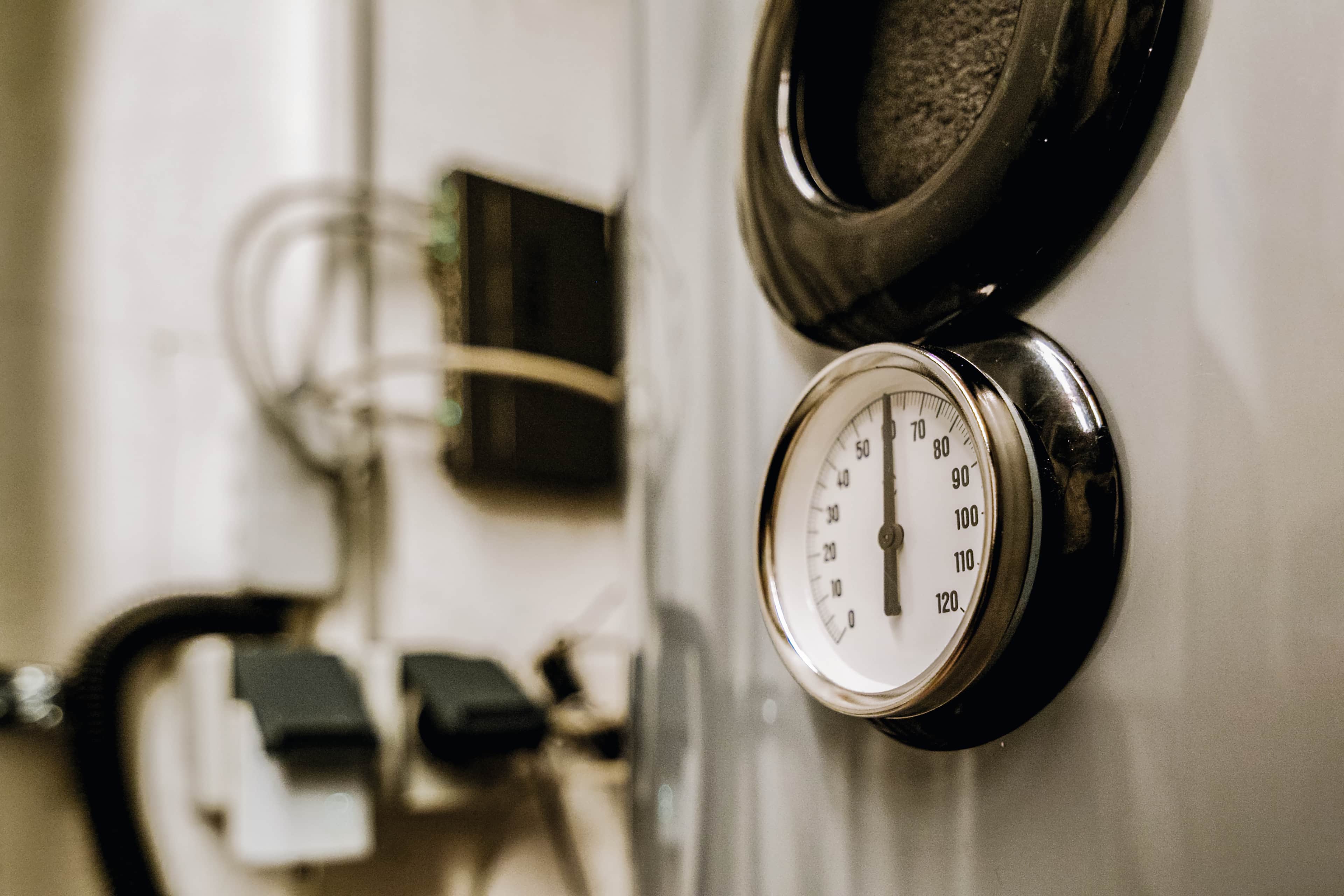 Lähikuva pyöreästä painemittarista teollisuuslaitteessa, asteikko 0:sta 120:een. Taustalla näkyy johtoja ja liittimiä.