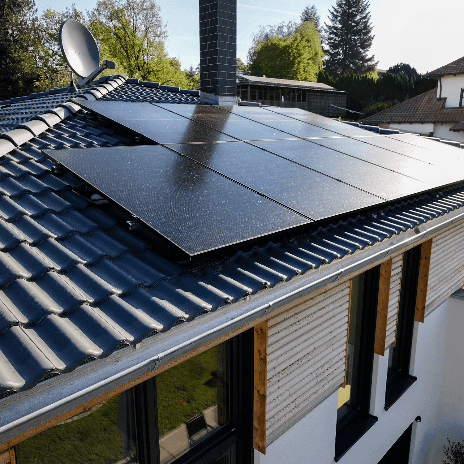 Modernin talon katolla on aurinkopaneelit, ja sitä ympäröivät puut. Katolla on myös savupiippu ja satelliittiantenni.