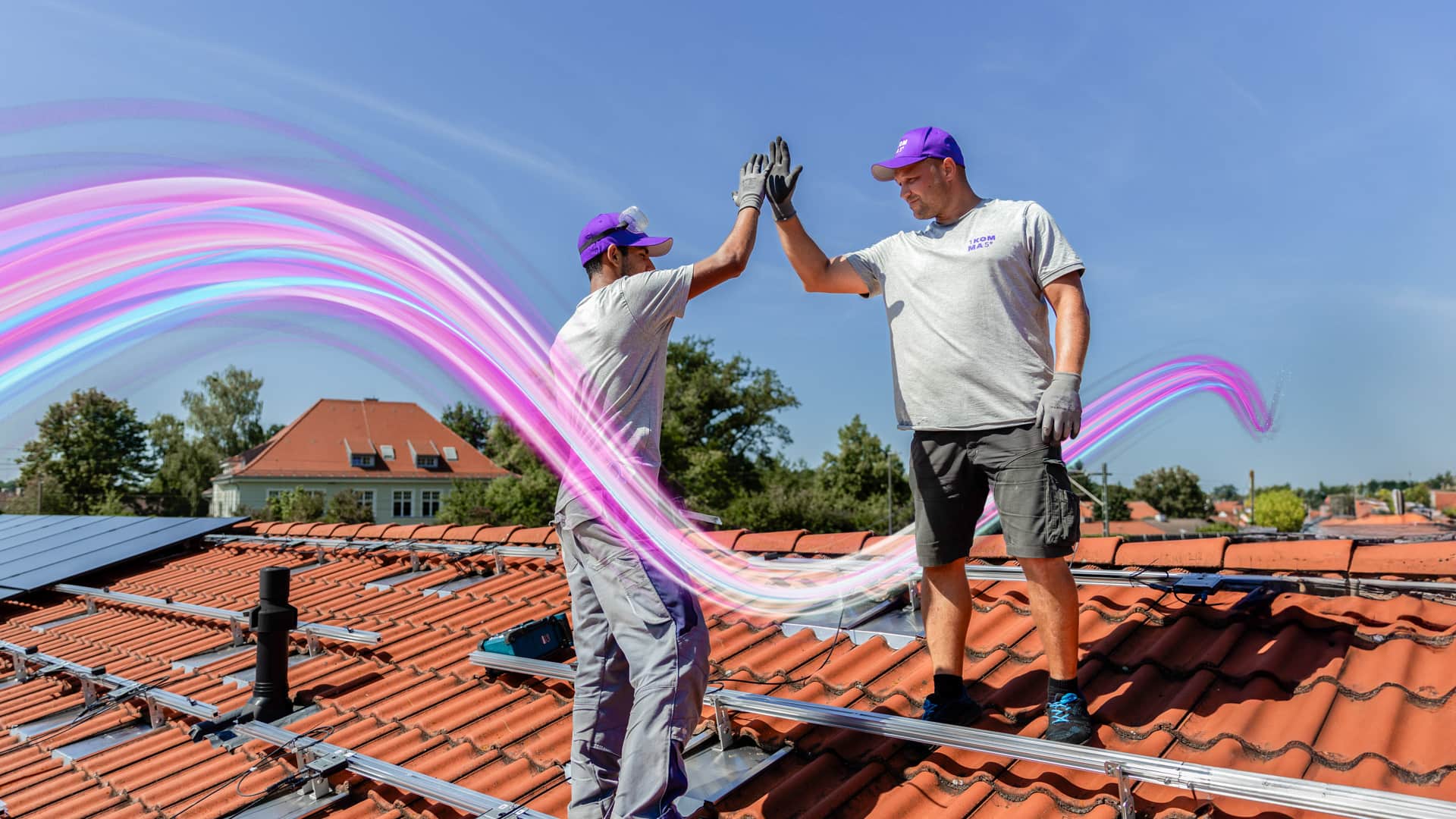 Kaksi työntekijää violetit lippikset päässään antaa yläfemmat tiilikatolla, jossa on aurinkopaneelit, kirkkaan sinisen taivaan alla. Heidän välillään kaartuu pinkki ja violetti energiaalto.