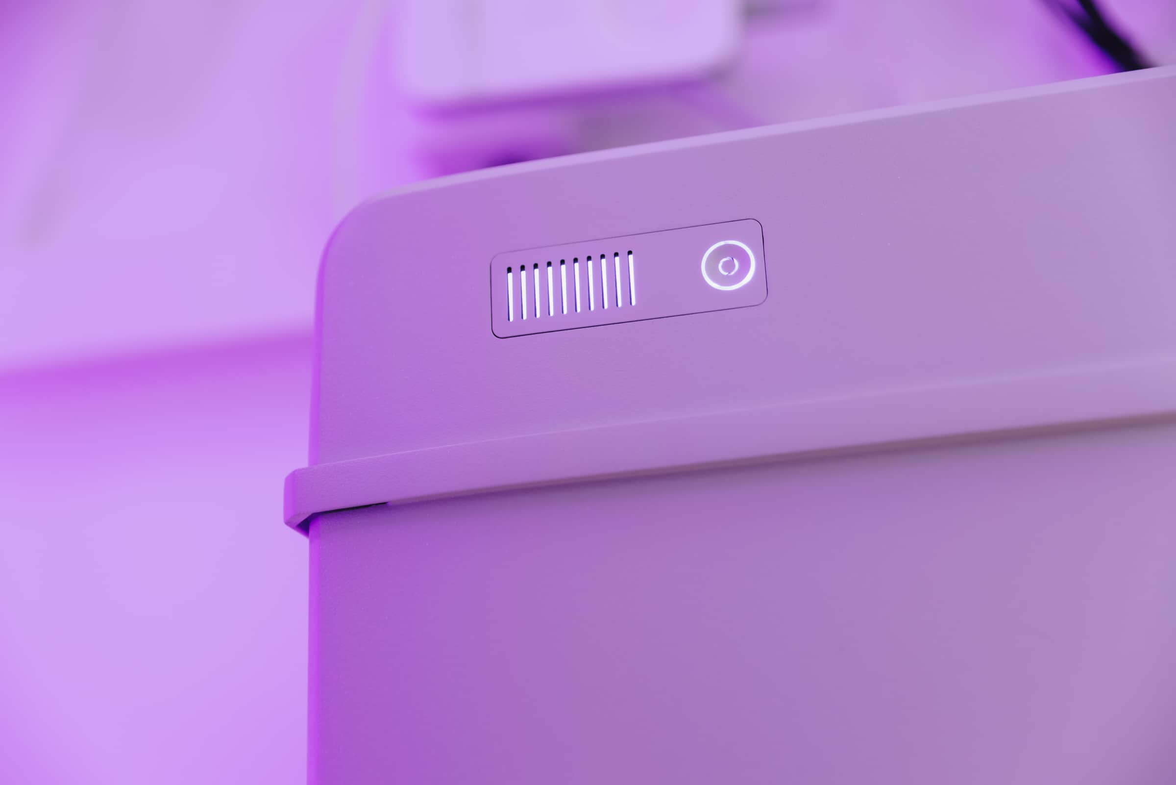 Lähikuva aurinkoenergian varastointiyksiköstä, jossa on hehkuva virtapainike ja ilmanvaihtoaukko, valaistuna violetilla valolla.