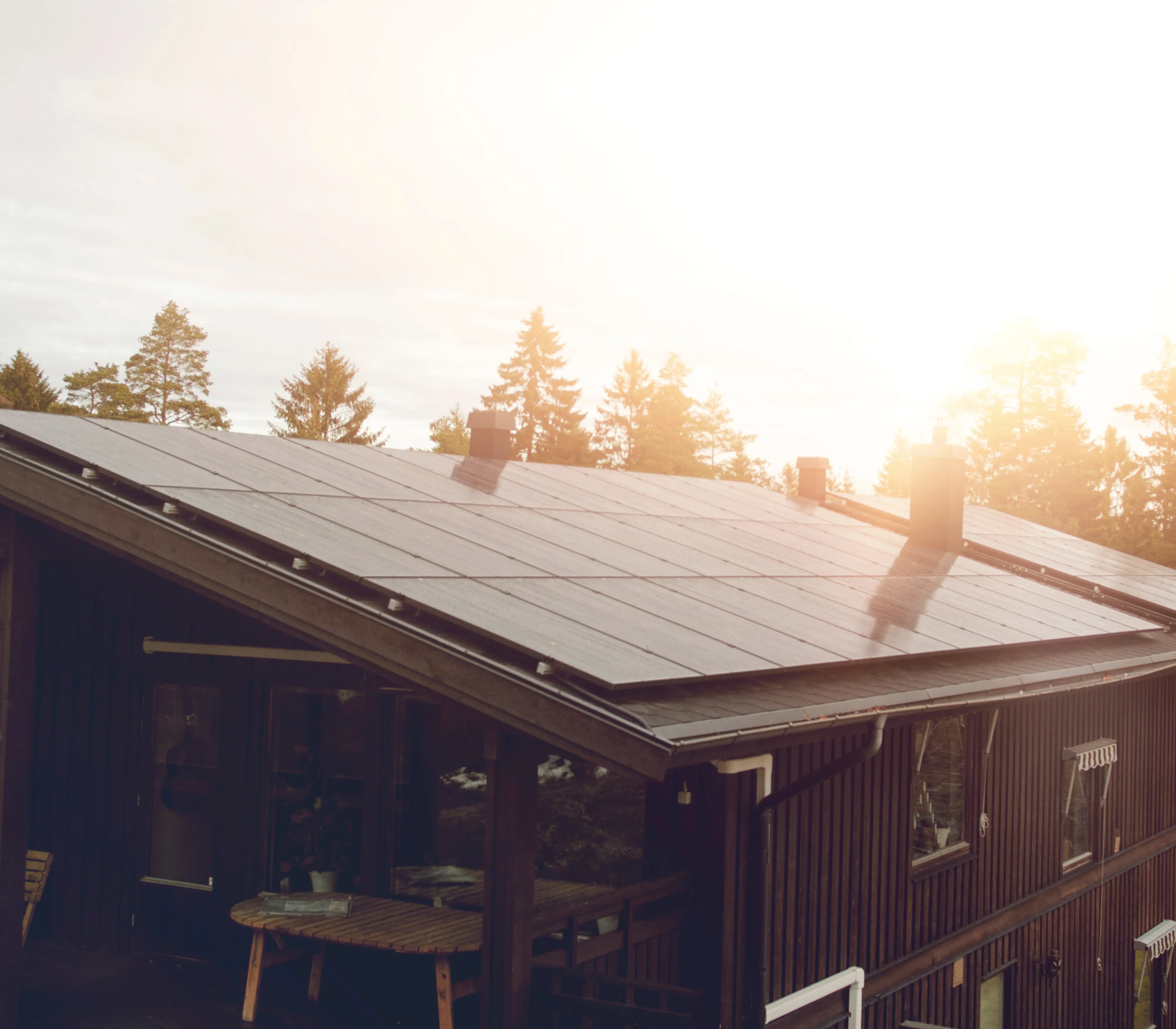 Auringonvalossa kylpevä talo, jonka katolla on aurinkopaneelit, puiden ympäröimänä. Auringonvalo luo lämpimän hehkun maisemaan.