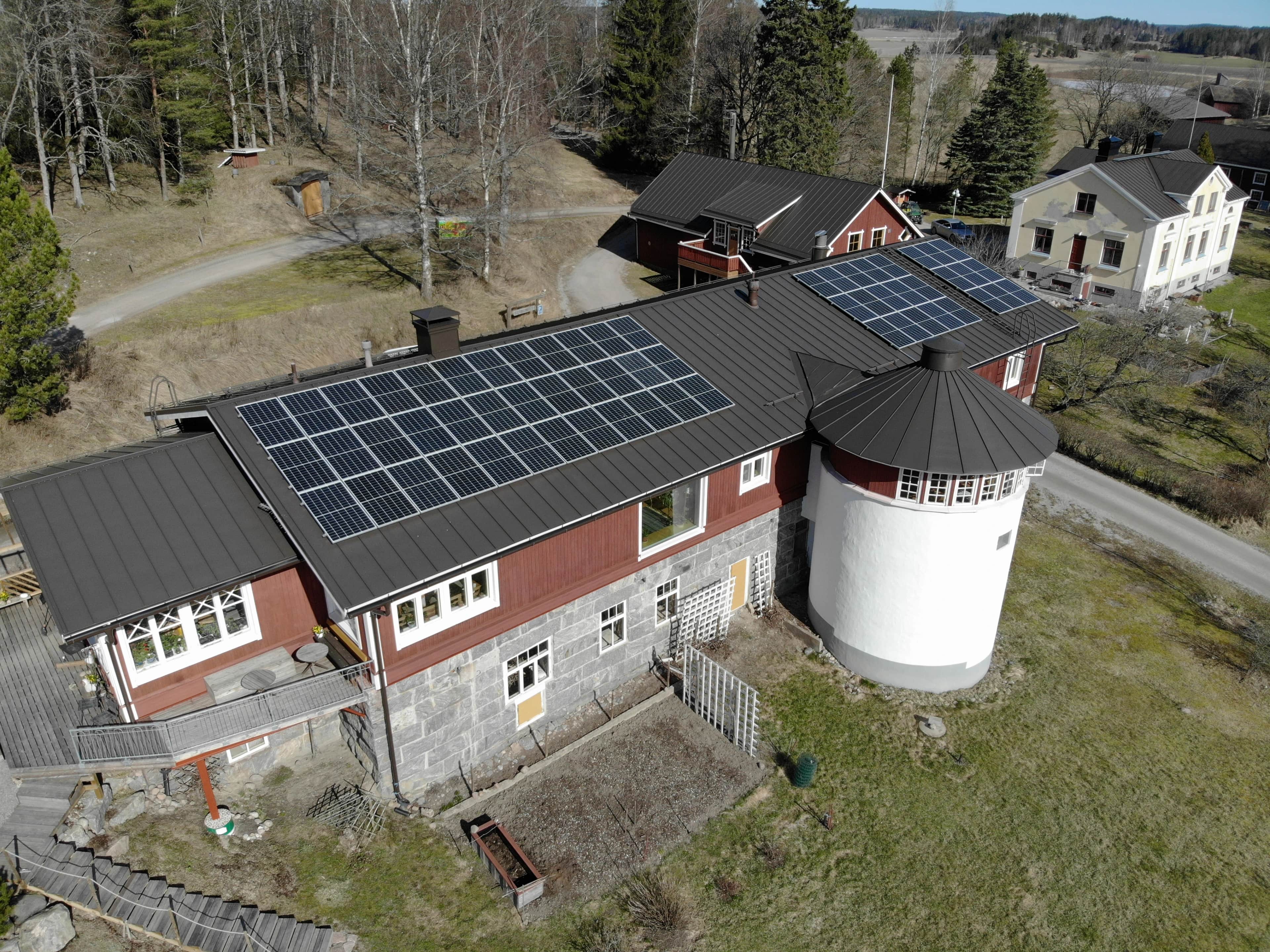 Ilmakuva punaisesta maalaistalosta, jonka metallikatto on peitetty aurinkopaneeleilla ja jossa on kiinni valkoinen siilon kaltainen torni.