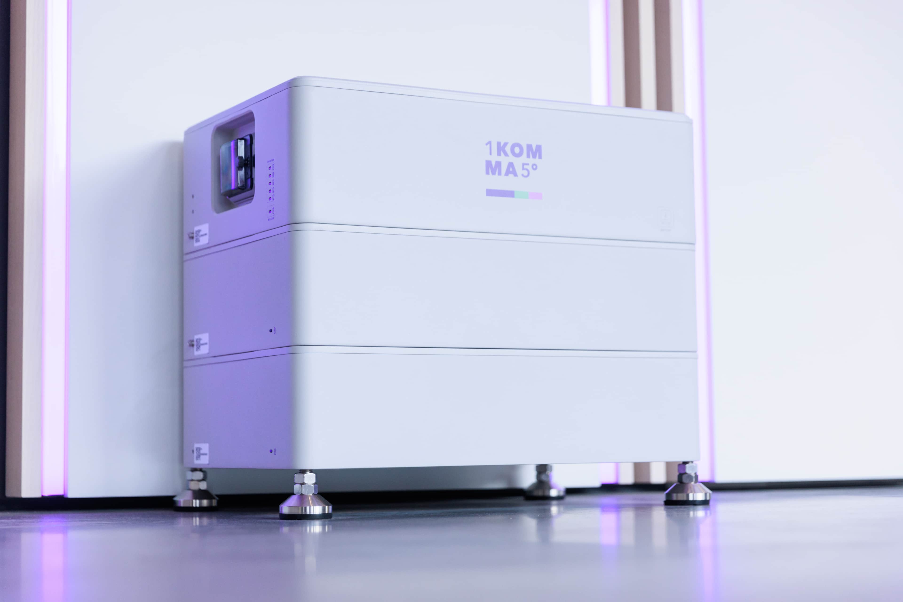 Tyylikäs, moderni virtavarastointilaite, jossa on "1KOMMA5°"-merkintä, on sijoitettu sileälle lattialle säädettävillä jaloilla.