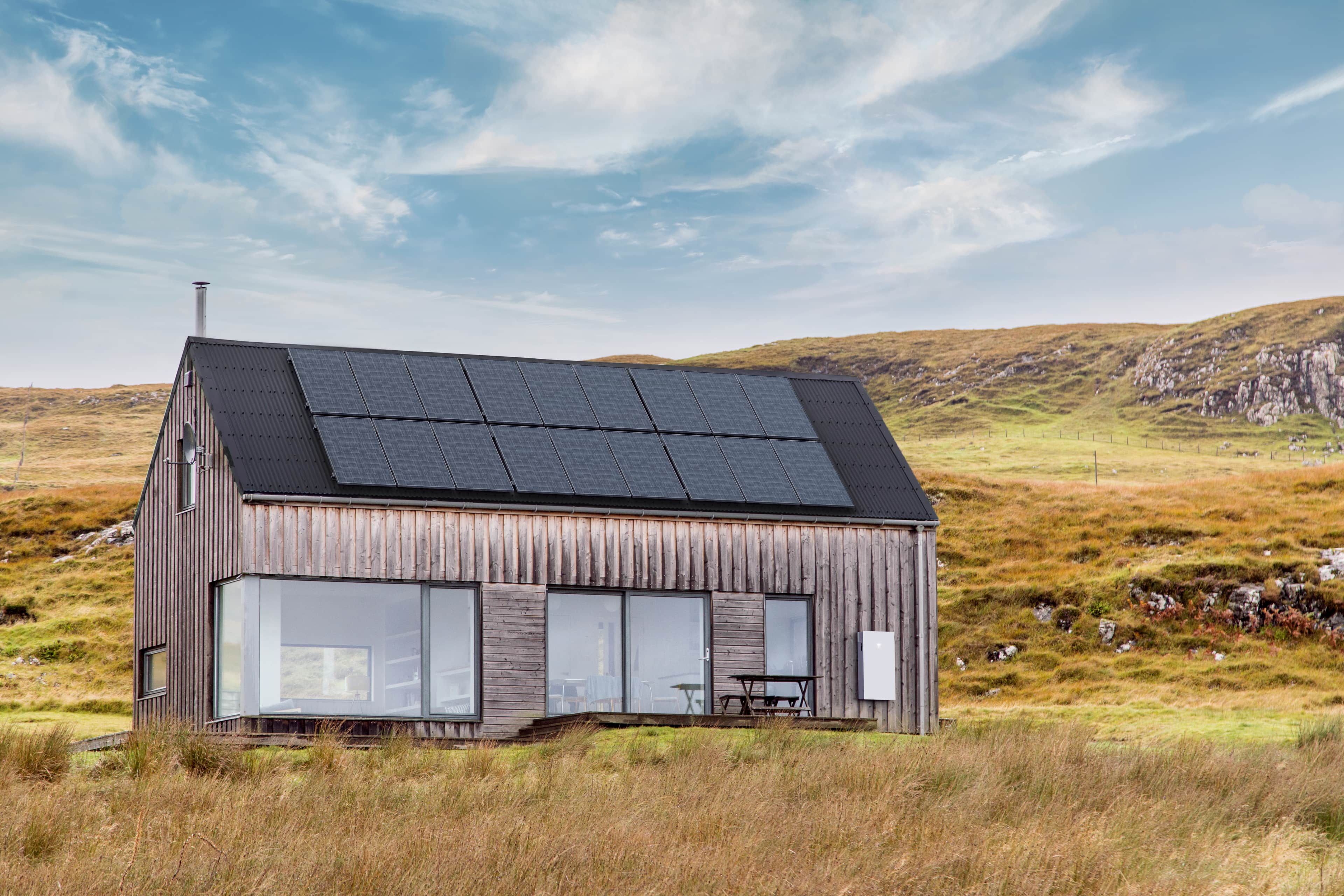 modern sustainable home with solar panels on the roof situated in a scenic, grassy landscape under a partly cloudy sky