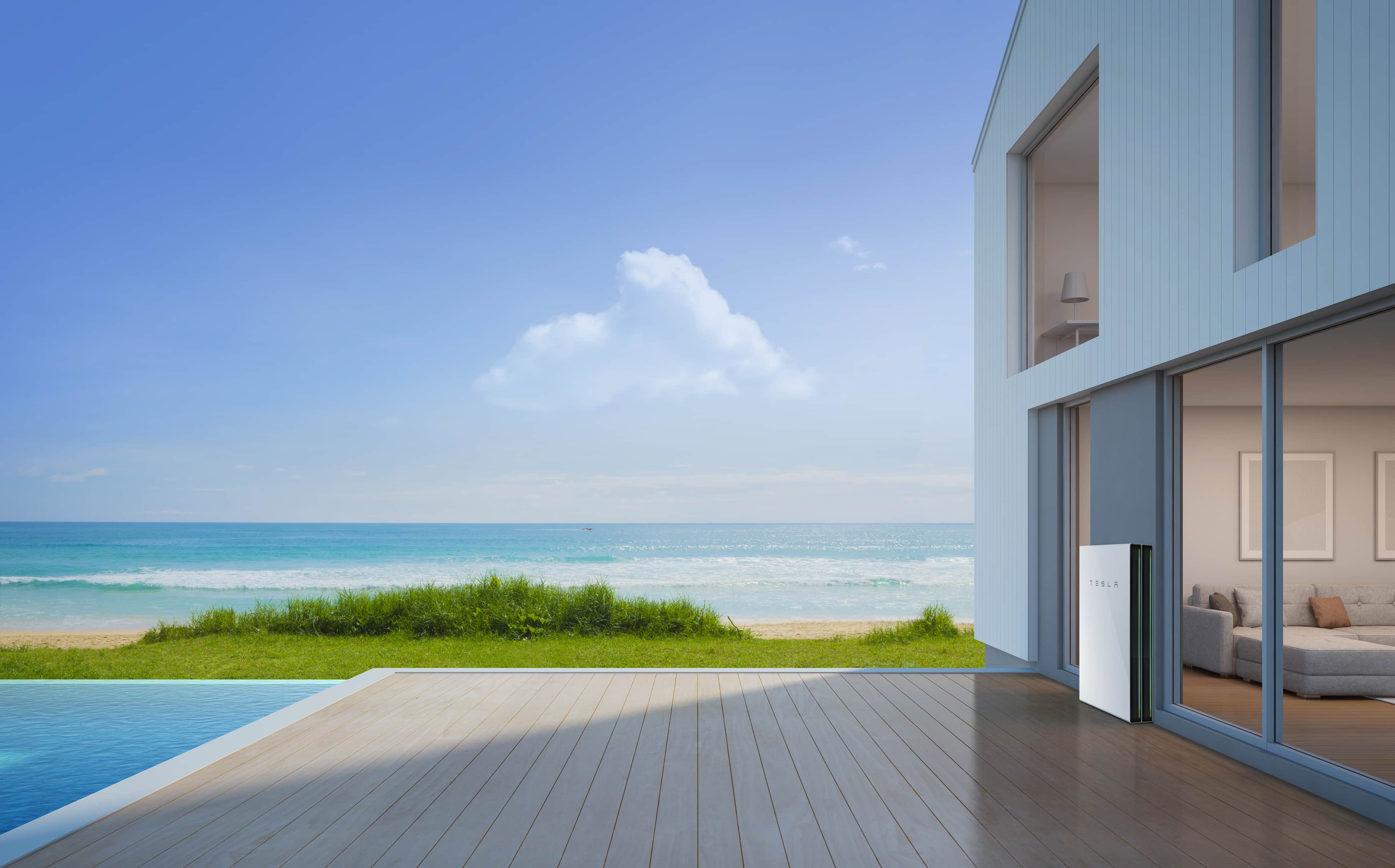 A Tesla Powerwall 2 mounted on a wall outside a modern seaside home with a wooden deck