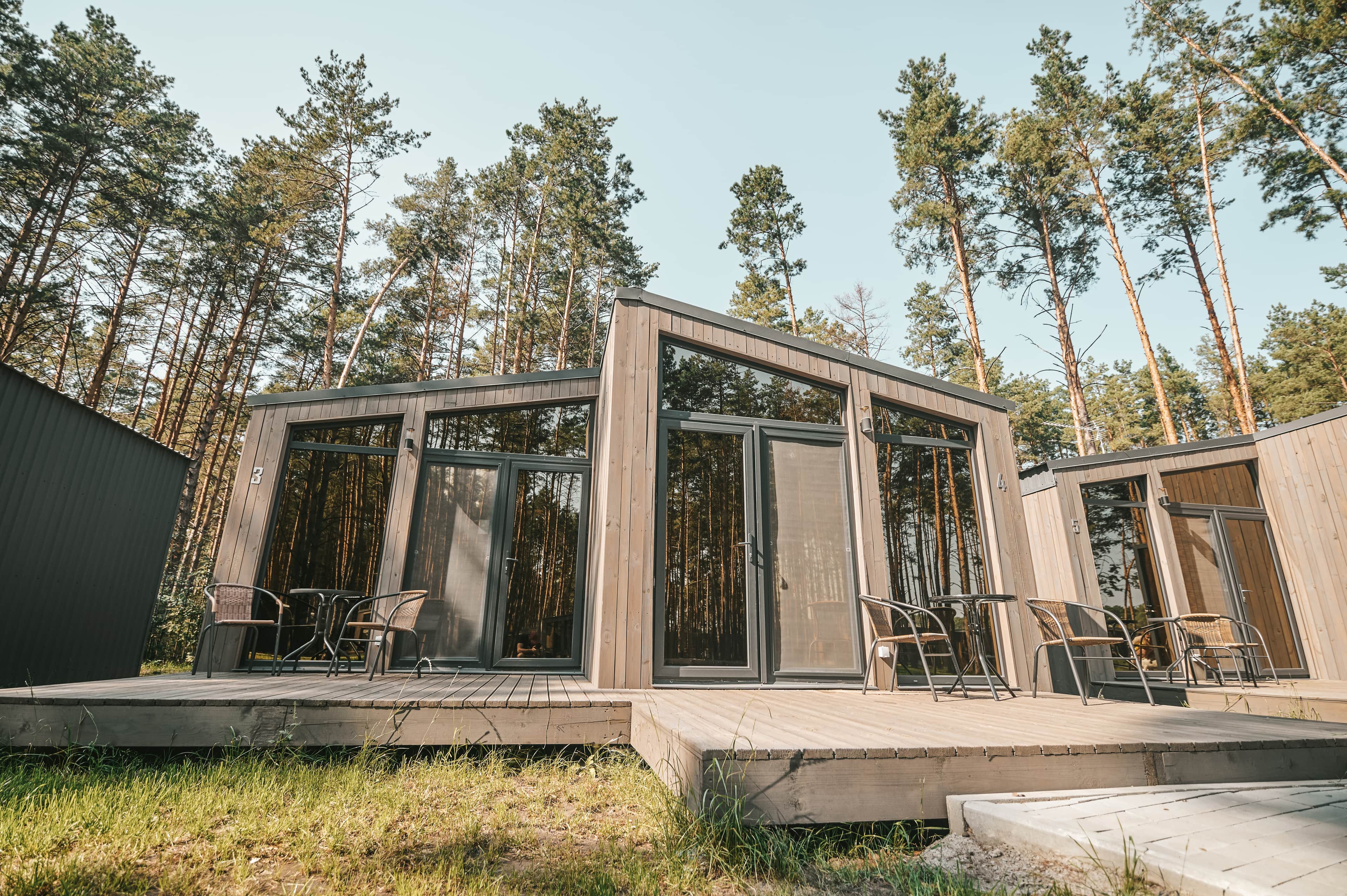 Modernit puiset mökit suurilla lasi-ikkunoilla ja terasseilla, jotka sijaitsevat metsäisessä ympäristössä korkeiden mäntyjen keskellä.